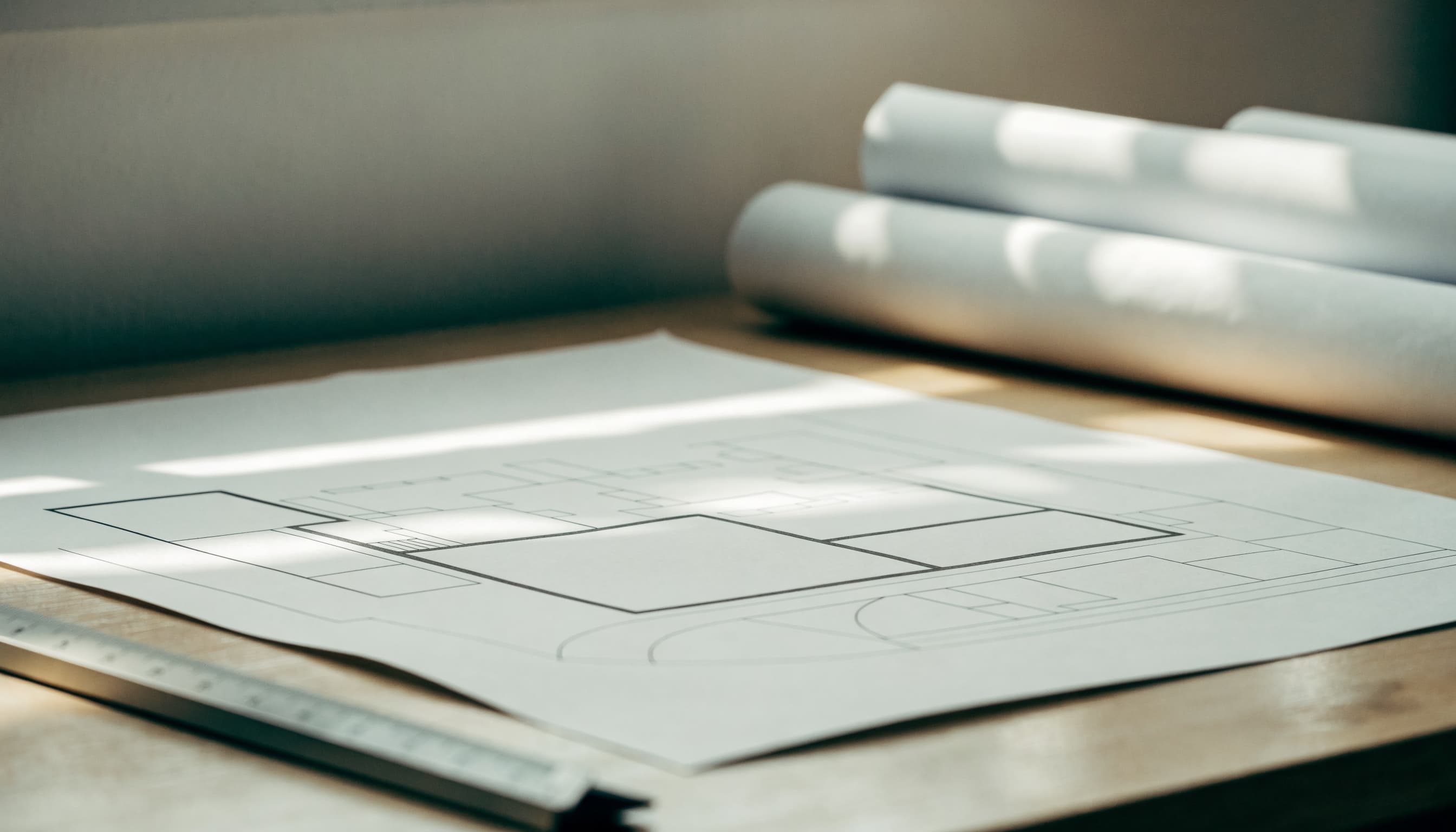 An architect's site layout drawing on a desk with a scale rule, lit by raking daylight